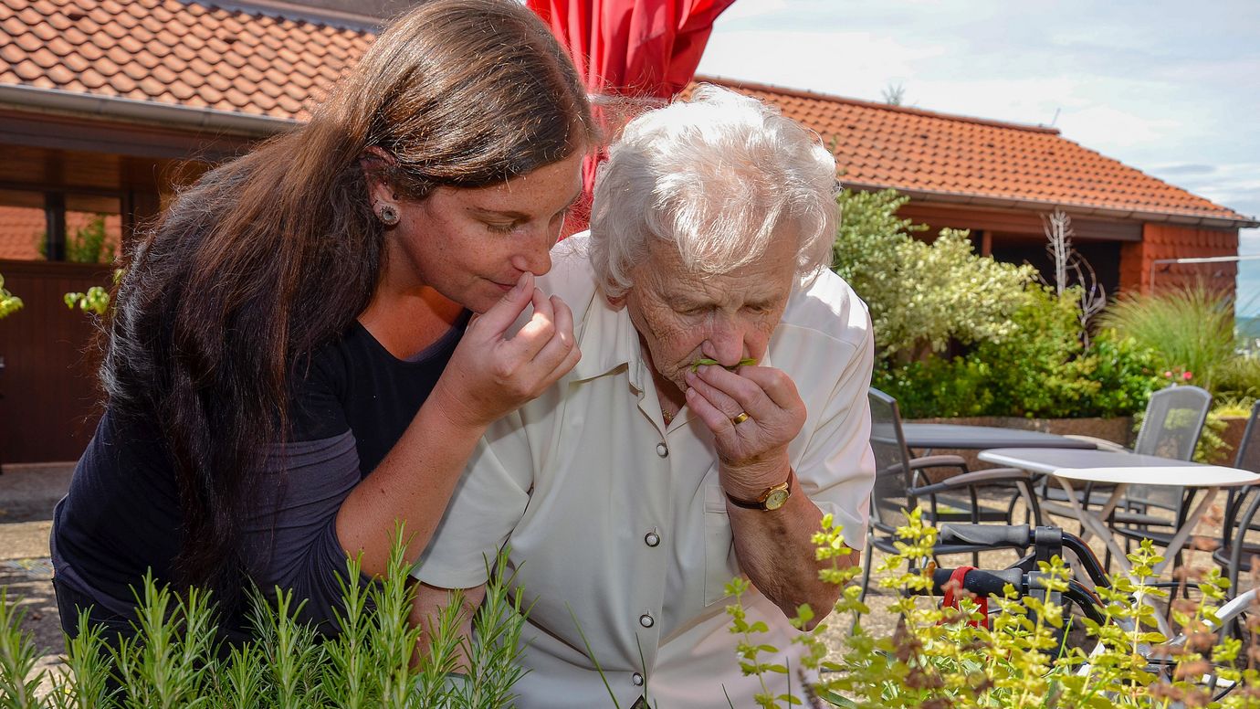 Betreuerin und Seniorin riechen an Kräutern