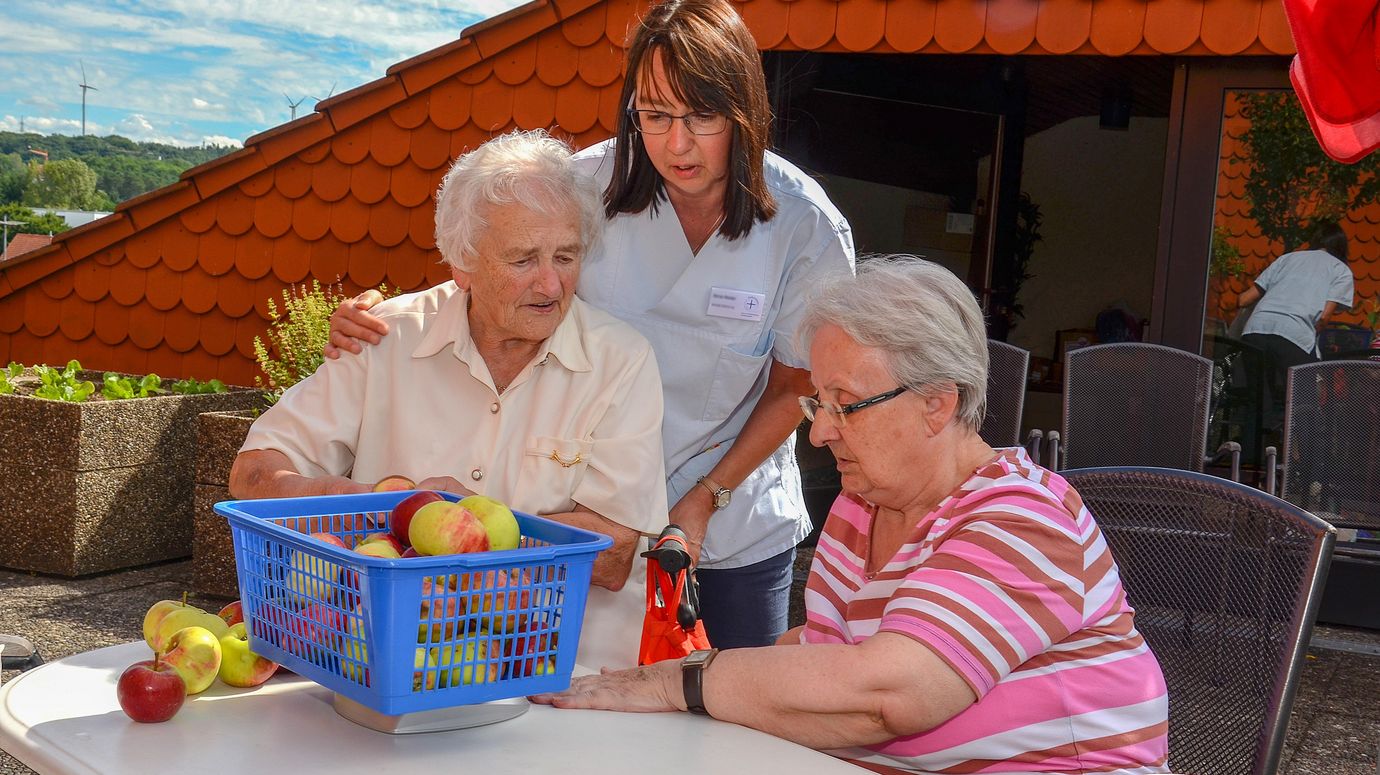 Betreuerin wiegt mit Seniorinnen Äpfel