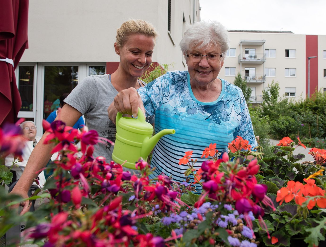 Seniorin gießt mit Pflegerin Blumen