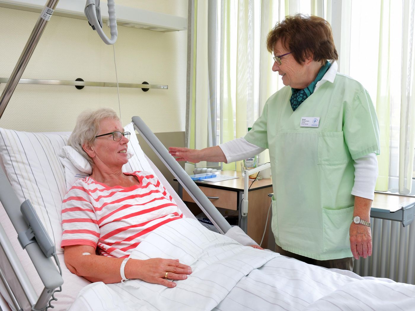 Grüne Dame im Gespräch mit Patienten am Krankenbett