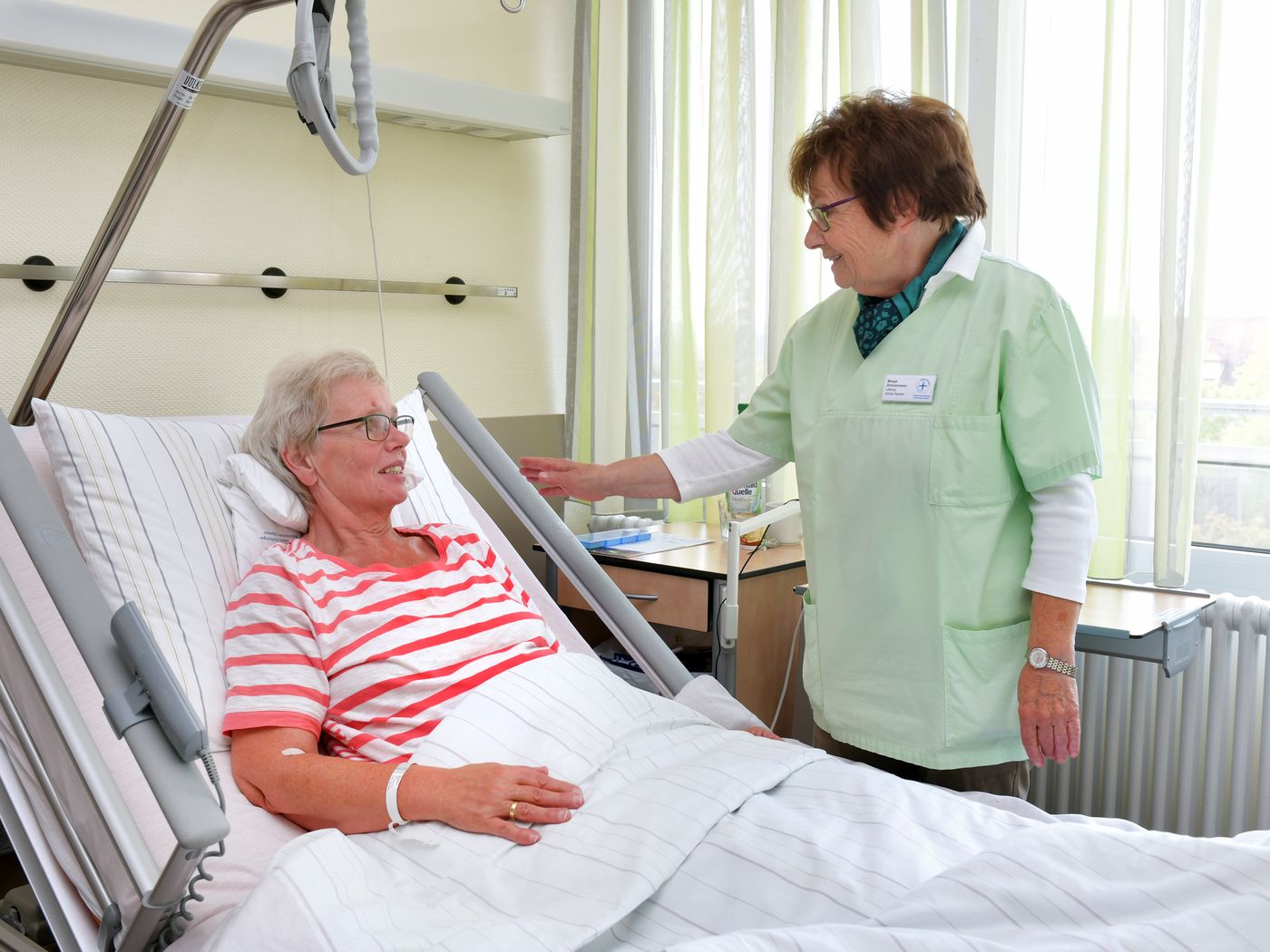 Grüne Dame im Gespräch mit Patienten am Krankenbett
