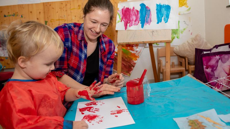 Erzieherin und Kind machen bei Händeabdruck mit roter Farbe