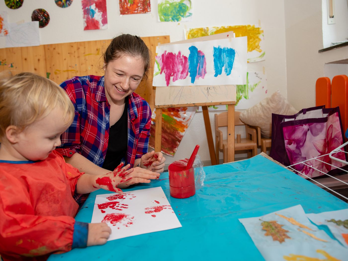 Erzieherin und Kind machen bei Händeabdruck mit roter Farbe