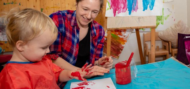 Erzieherin und Kind machen bei Händeabdruck mit roter Farbe