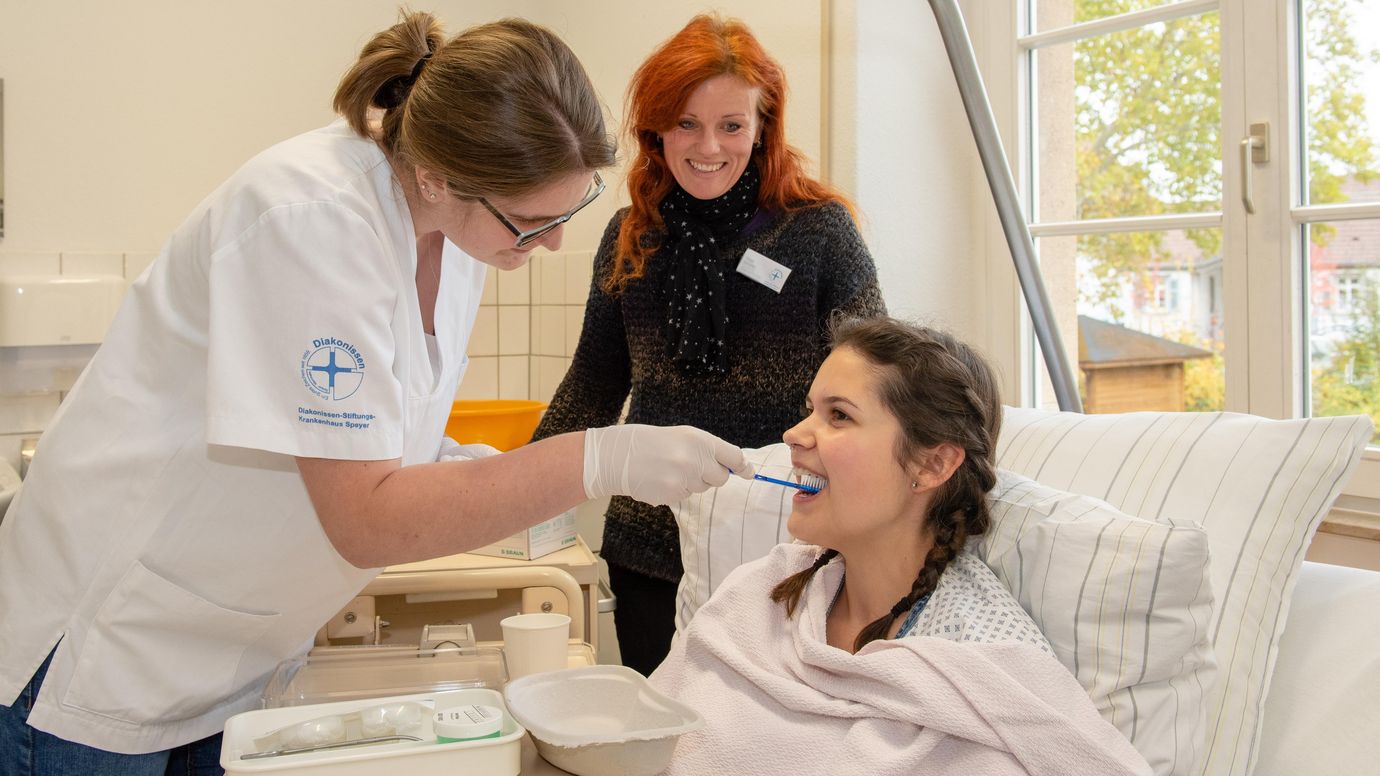 Pflegeschülerin übt Zähneputzen an Patientin