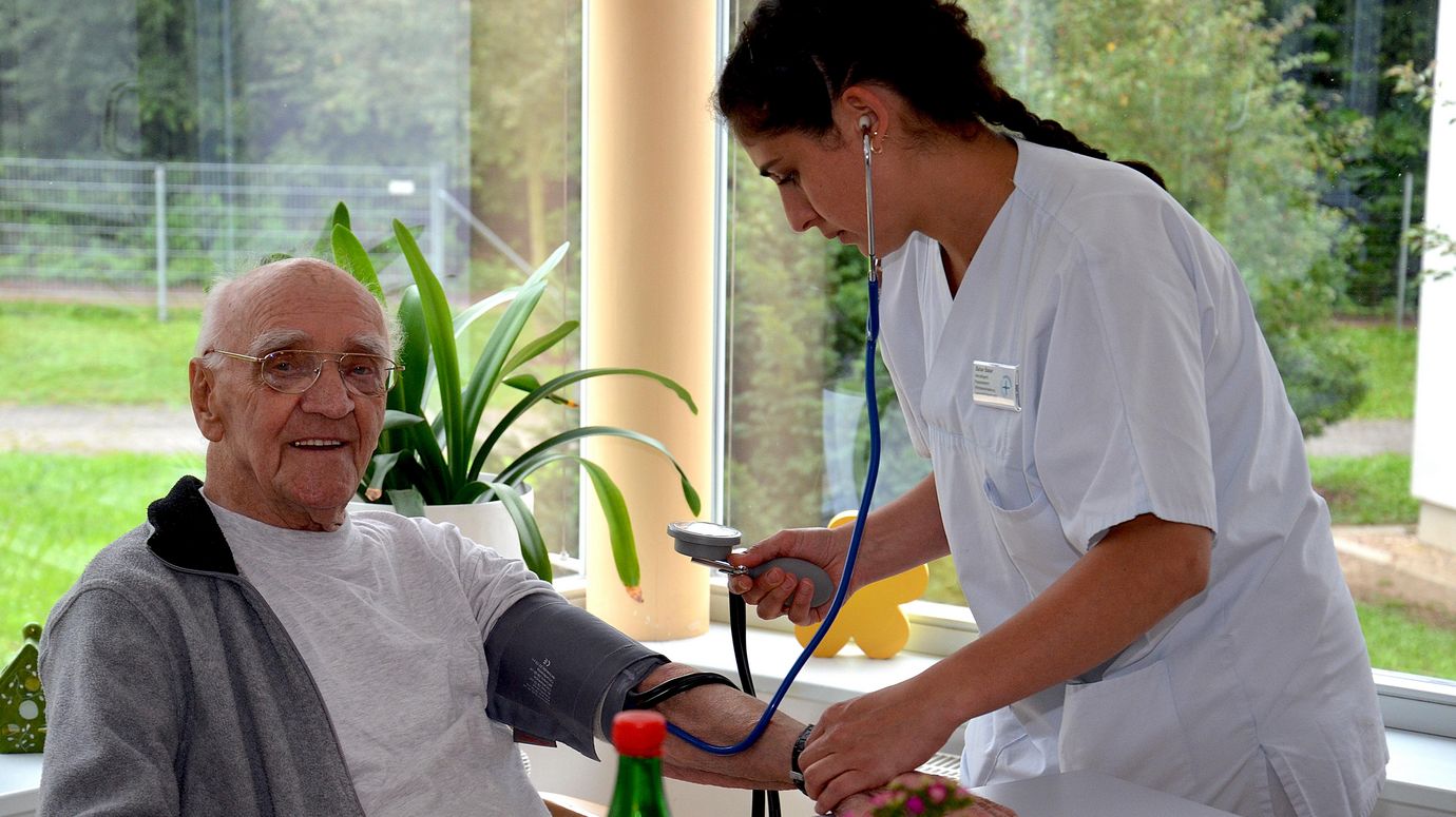 Pflegerin misst bei einem Senior den Blutdruck